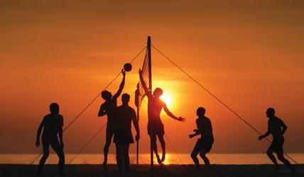 A group playing beach volleyball in the sunset.